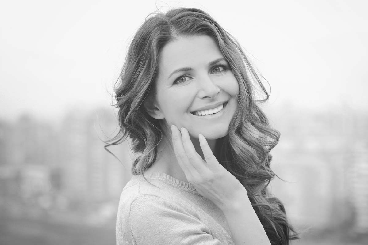 a woman smiles while touching her face after a facelift in Dallas, TX